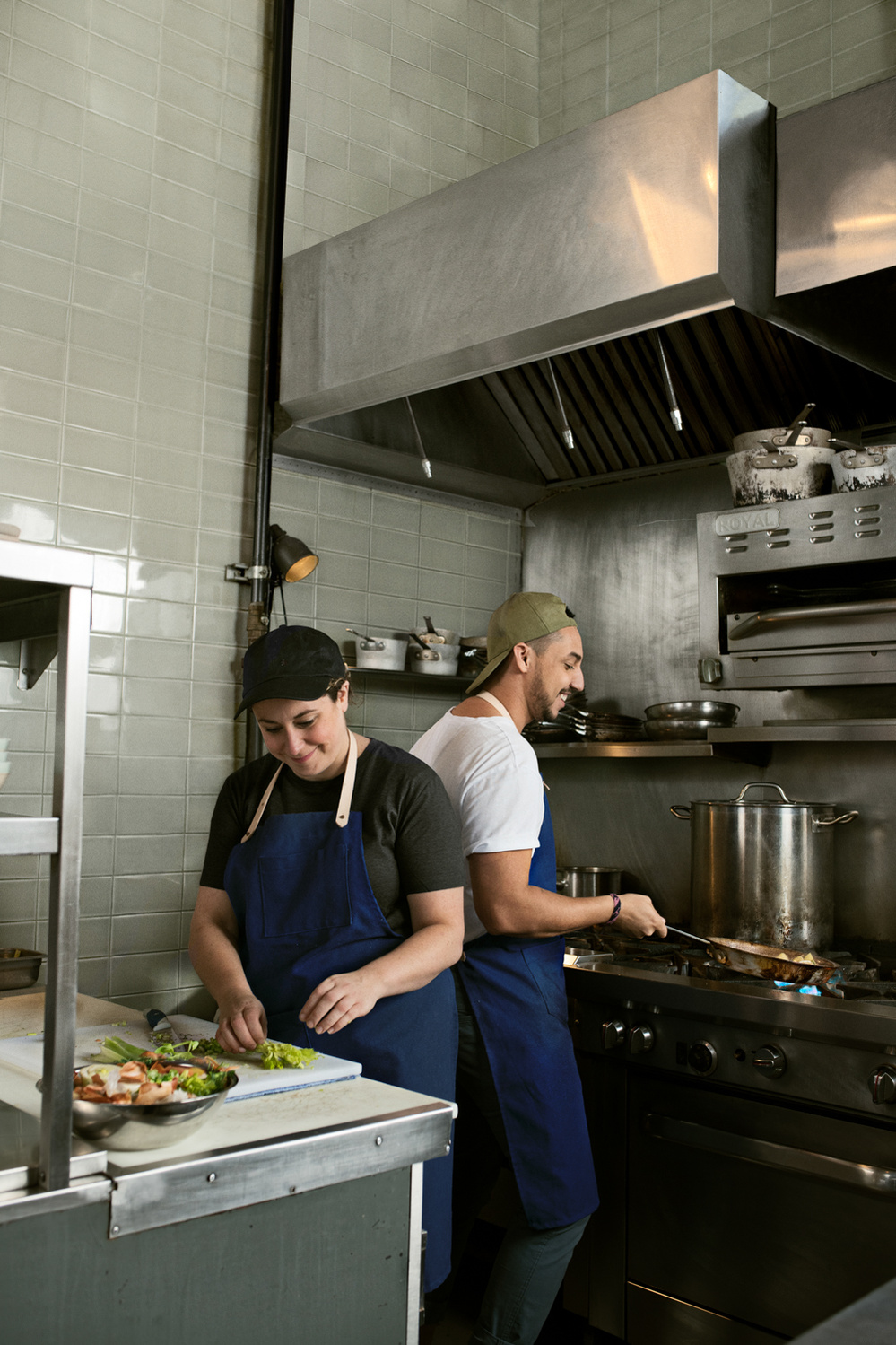 Deux cuisiniers dans une cuisine commerciale avec des tabliers bleus et des casquettes.