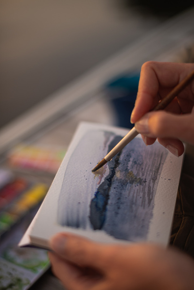 Main de femme réalisant une aquarelle de paysage.