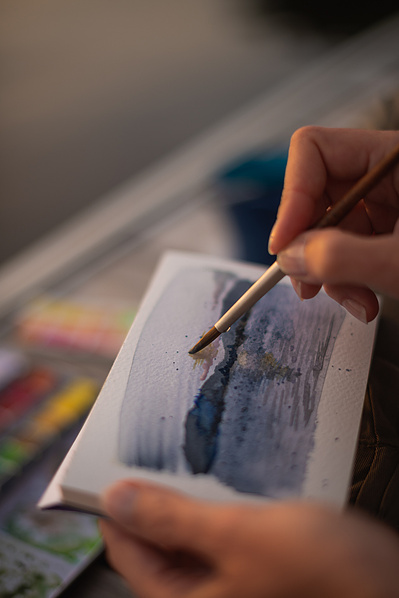 Main de femme réalisant une aquarelle de paysage.