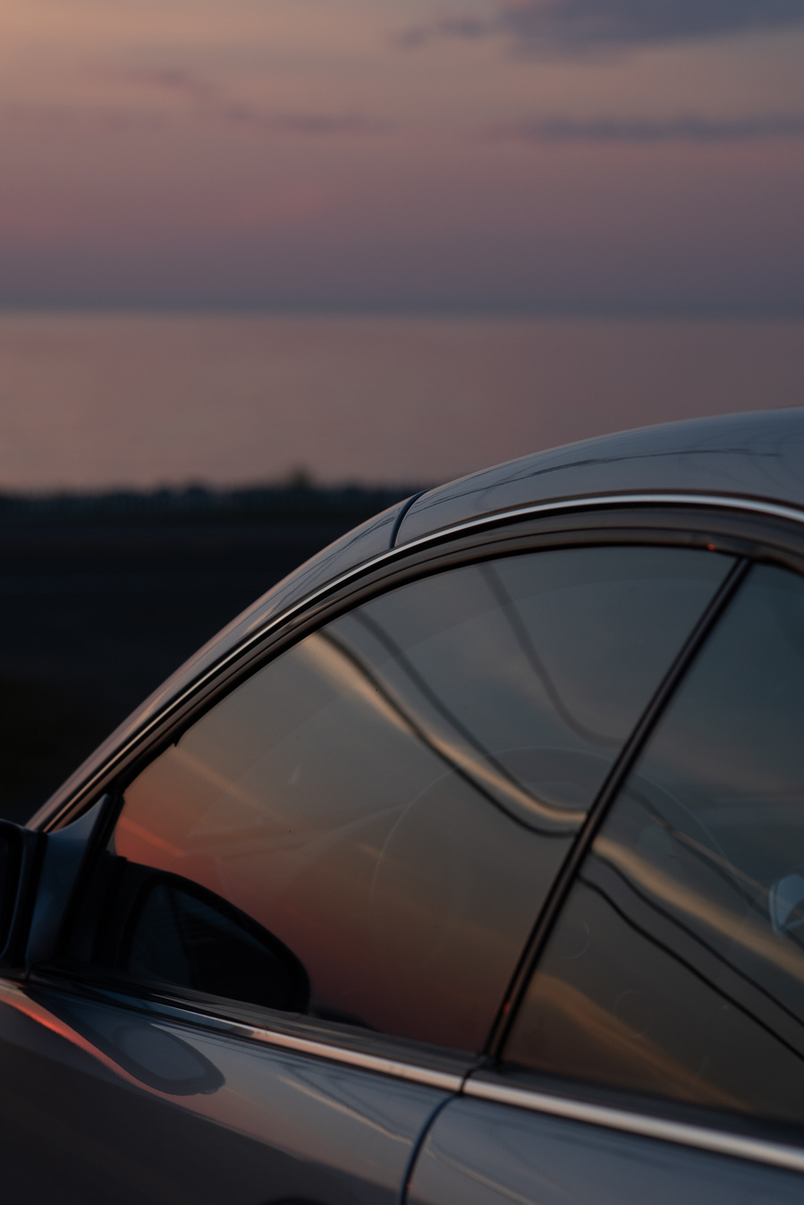 Reflets du coucher de soleil sur la vitre d'une voiture au bord de l'eau.