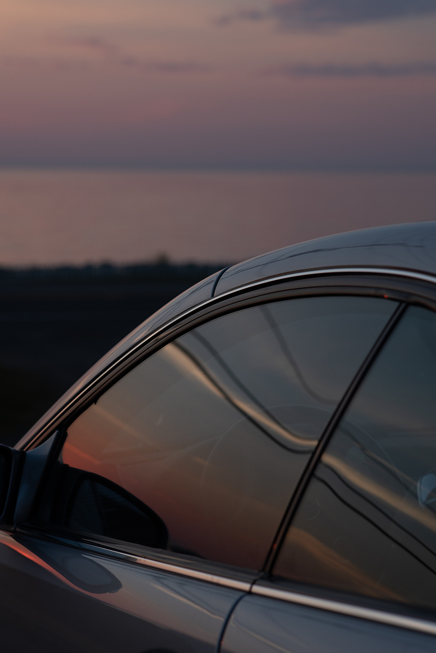 Reflets du coucher de soleil sur la vitre d'une voiture au bord de l'eau.
