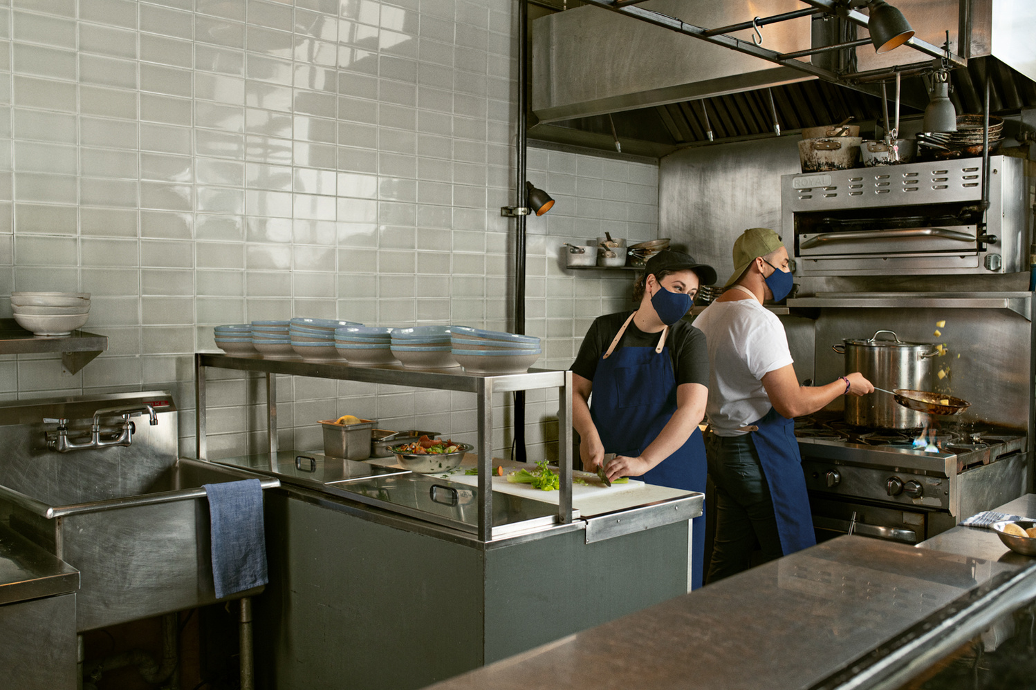 Deux cuisiniers de restaurant dos à dos portant des masques.
