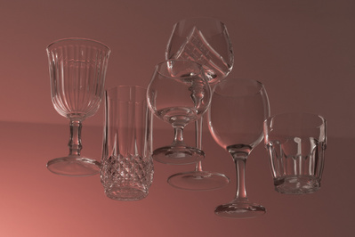 Verres variés vides semblant flotter sur fond rosé.