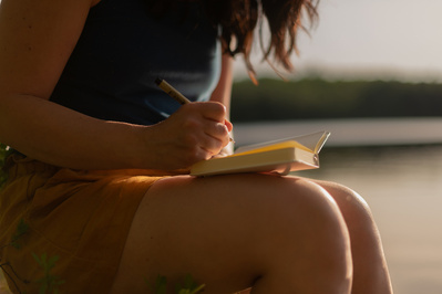 Femme dessinant dans un carnet au bord de l'eau en été.