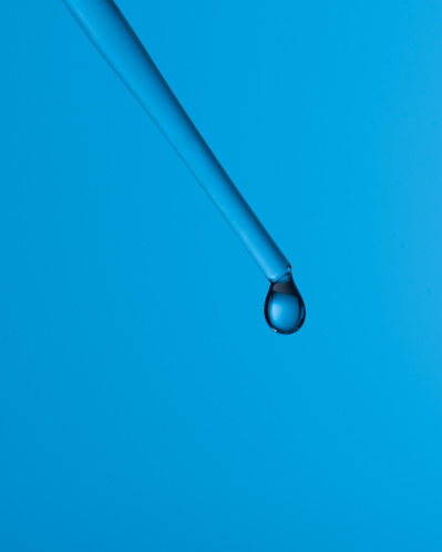 Goutte d'eau sortant d'une pipette sur fond bleu.
