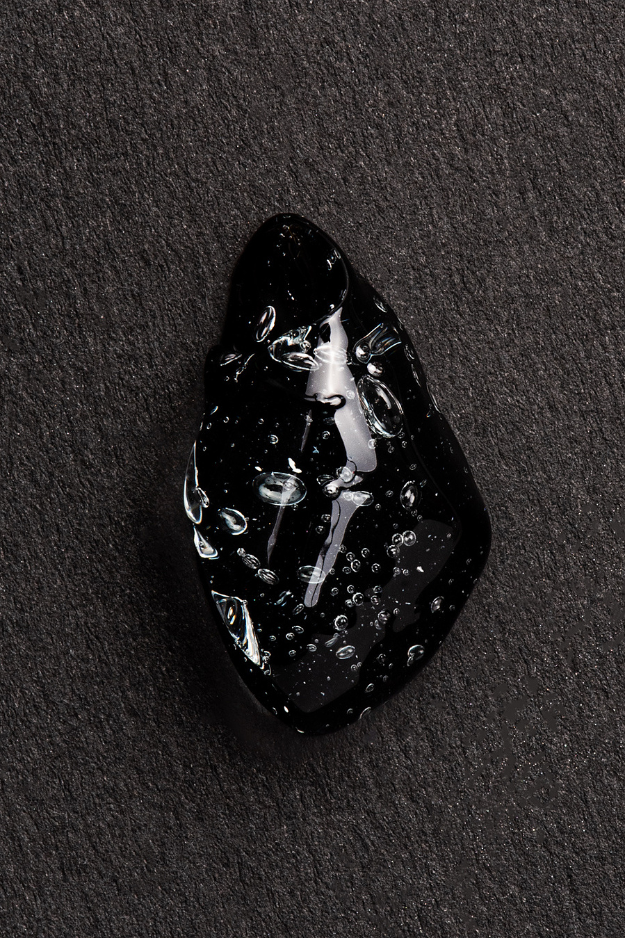 Texture de produit de beauté en gel contenant des bulles sur fond de papier noir.