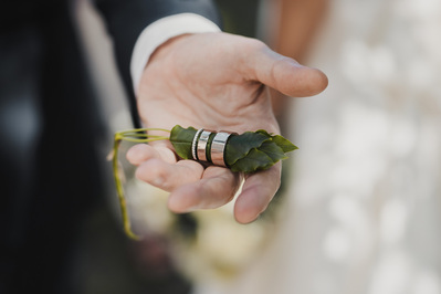 En man håller två vigselringar i sin hand, ringarna är vitt guld med vit sten och  är trädda i ett grönt löv.