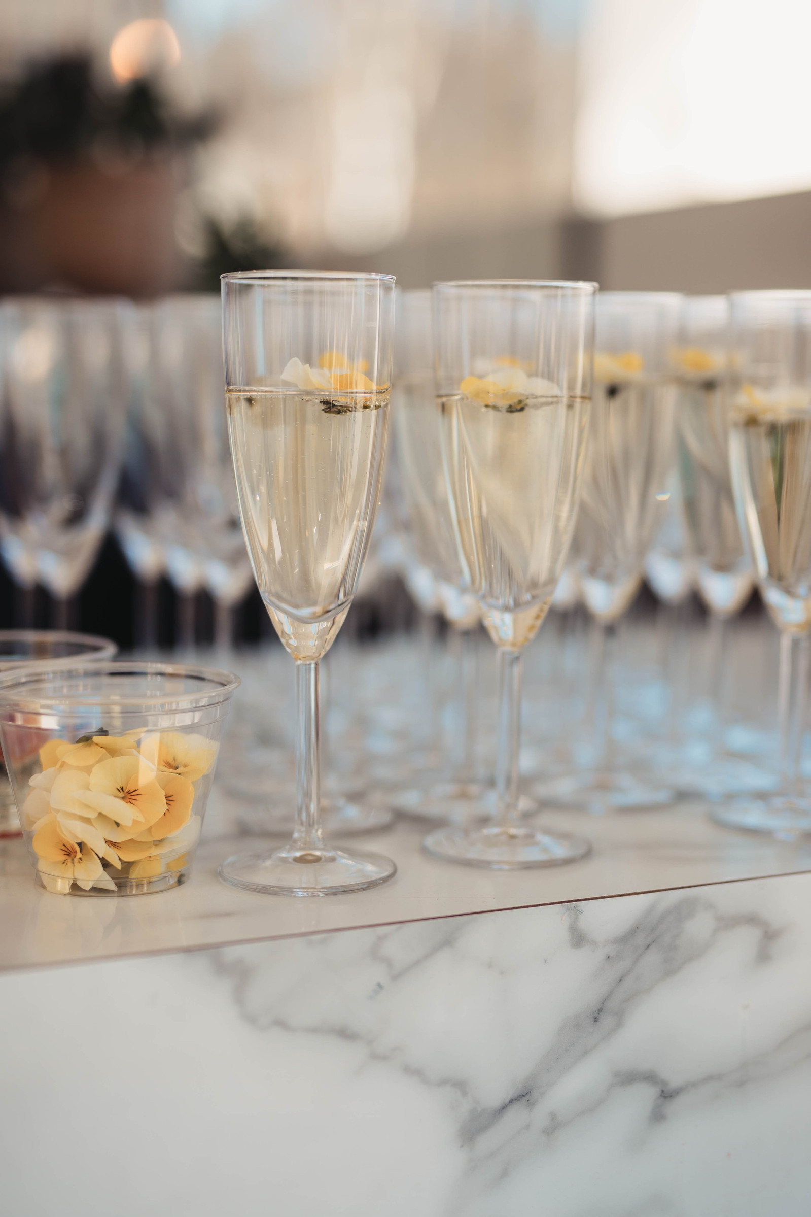 Champagne glas fyllda med bubbel och blomma på ett marmorbord. Vid sidan av gula blommor i ett vattenglas.