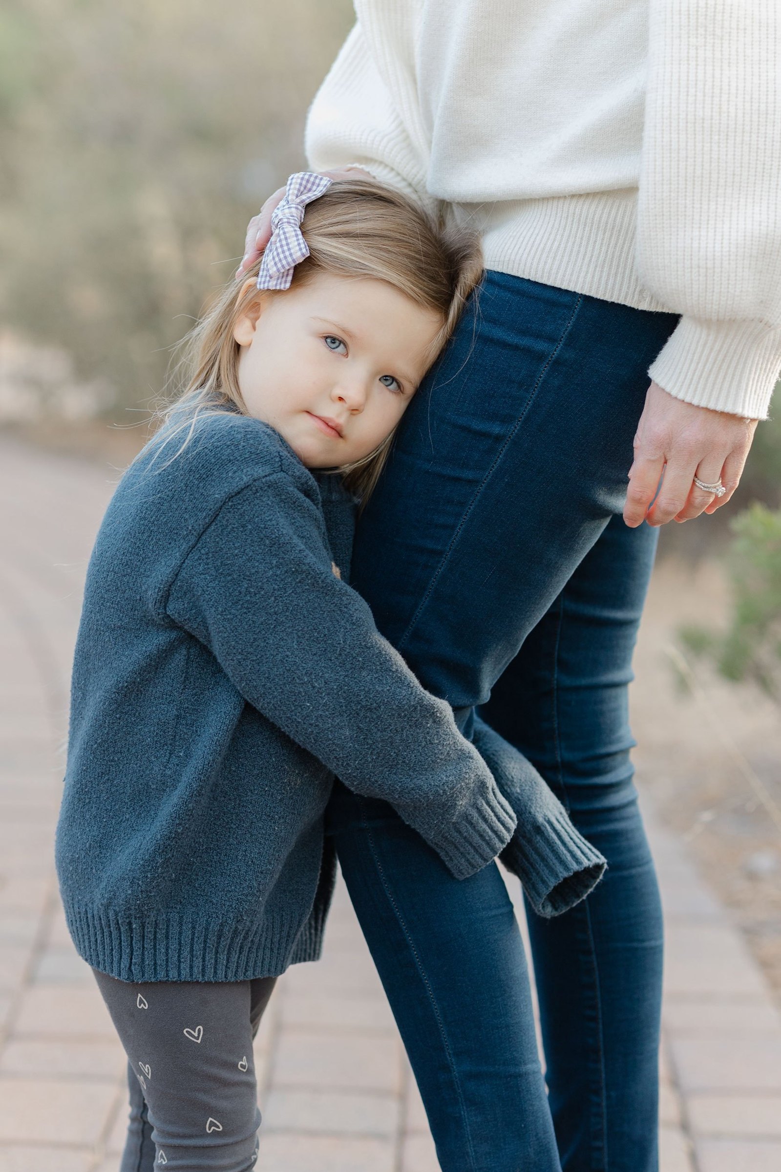 A sweet moment captured by the Lens Lady of a small child hugging her mother's leg during a family photo session. Keilah likes to capture all the small, emotive moments.