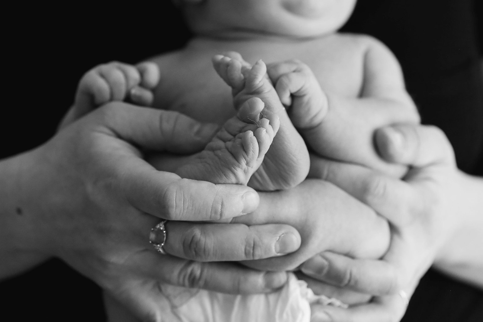 A classic black and white photo of mom's hands supporting and holding a newborn baby in an in-home newborn session in Prescott, AZ. The tiny newborn feet are the focus of the image.