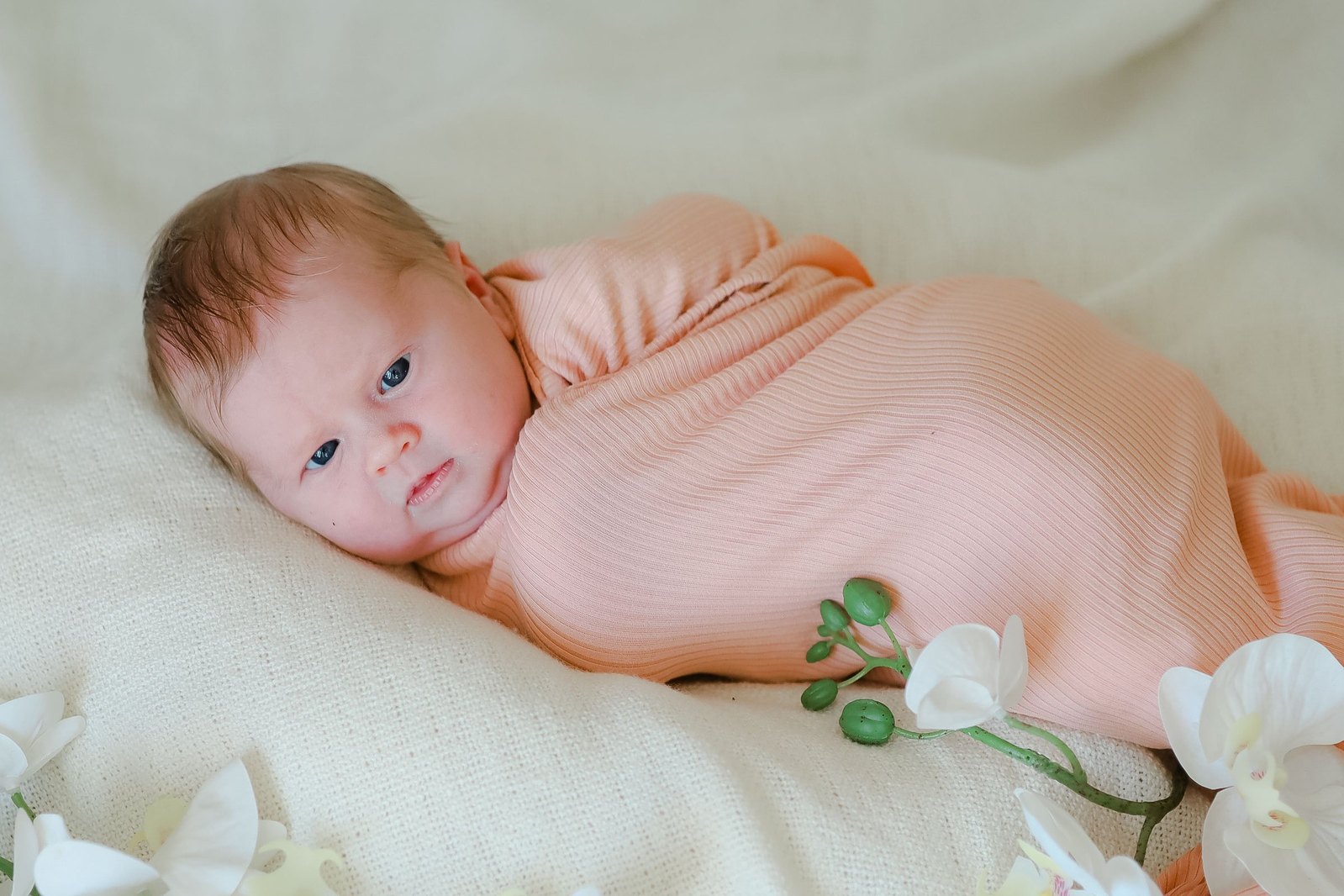 A bright and natural looking newborn girl swaddled on a bed with flowers captured in the Prescott area in an in-home newborn lifestyle session.