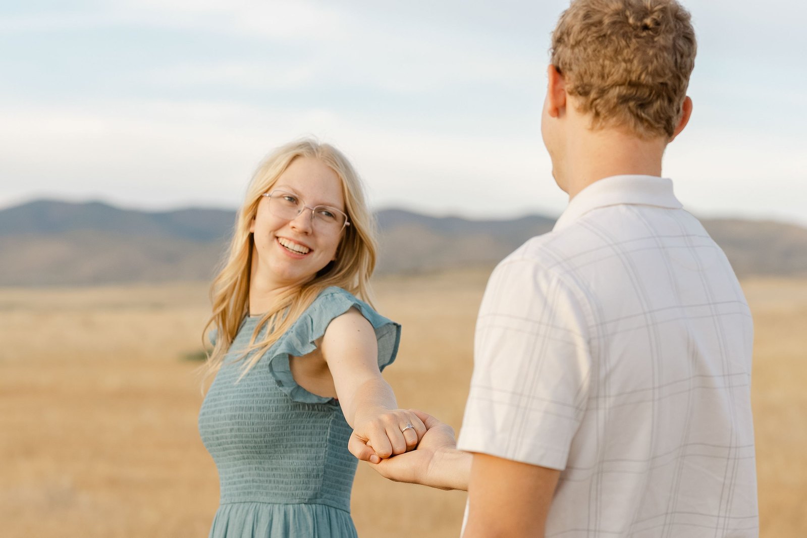 A newly engaged couple spinning in a field in Prescott Valley, AZ holding hands and showing off the engagement ring. The bride-to-be is radiant.