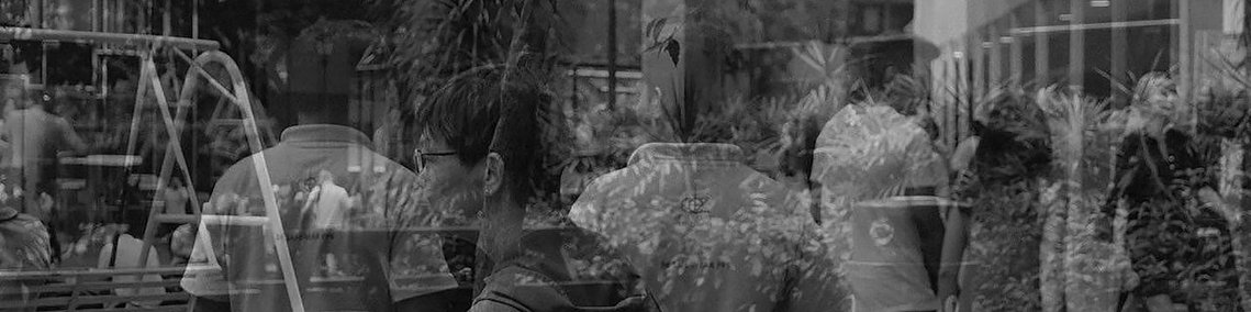 Dans une vitrine, on voit se refléter les passents et infrastructures et plantes de ce qui ressemble à un lieu public comme une université. L'architecture est moderne. On ressent quelque chose de l'ordre de l'anonymat dans la masse. 