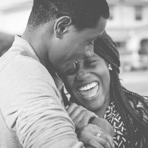 Un couple de jeunes gens, un homme et une femme noire, sont enlacés et rient ensemble. Elle porte des tresses et semble rire aux éclats. Le bonheur et la joie se dégage de ce portrait. 