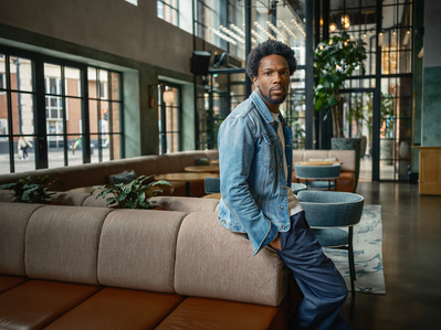 Portrait of actor Tosin Cole leading on a sofa in a London Hotel.