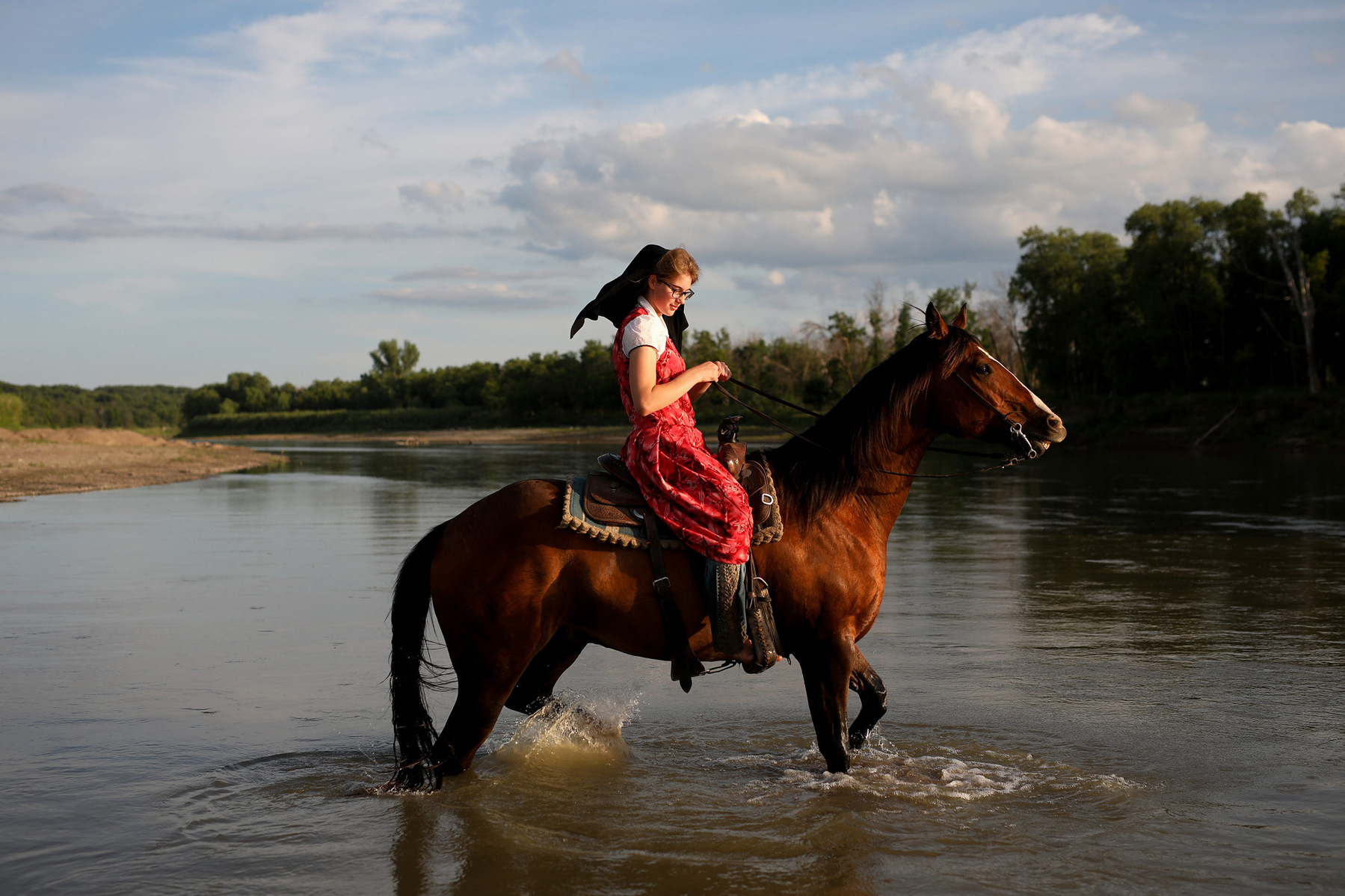 A Hutterite woman rides her horse through a river.
