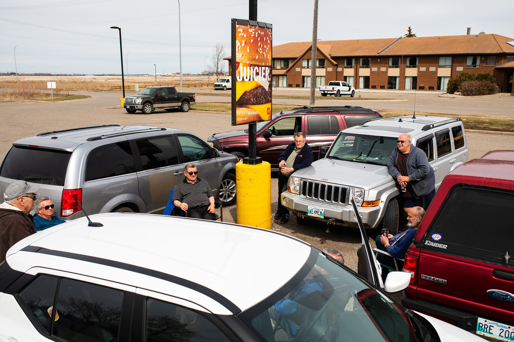 A group of men enjoy coffee in lawn chairs in a McDonald's parking lot.
