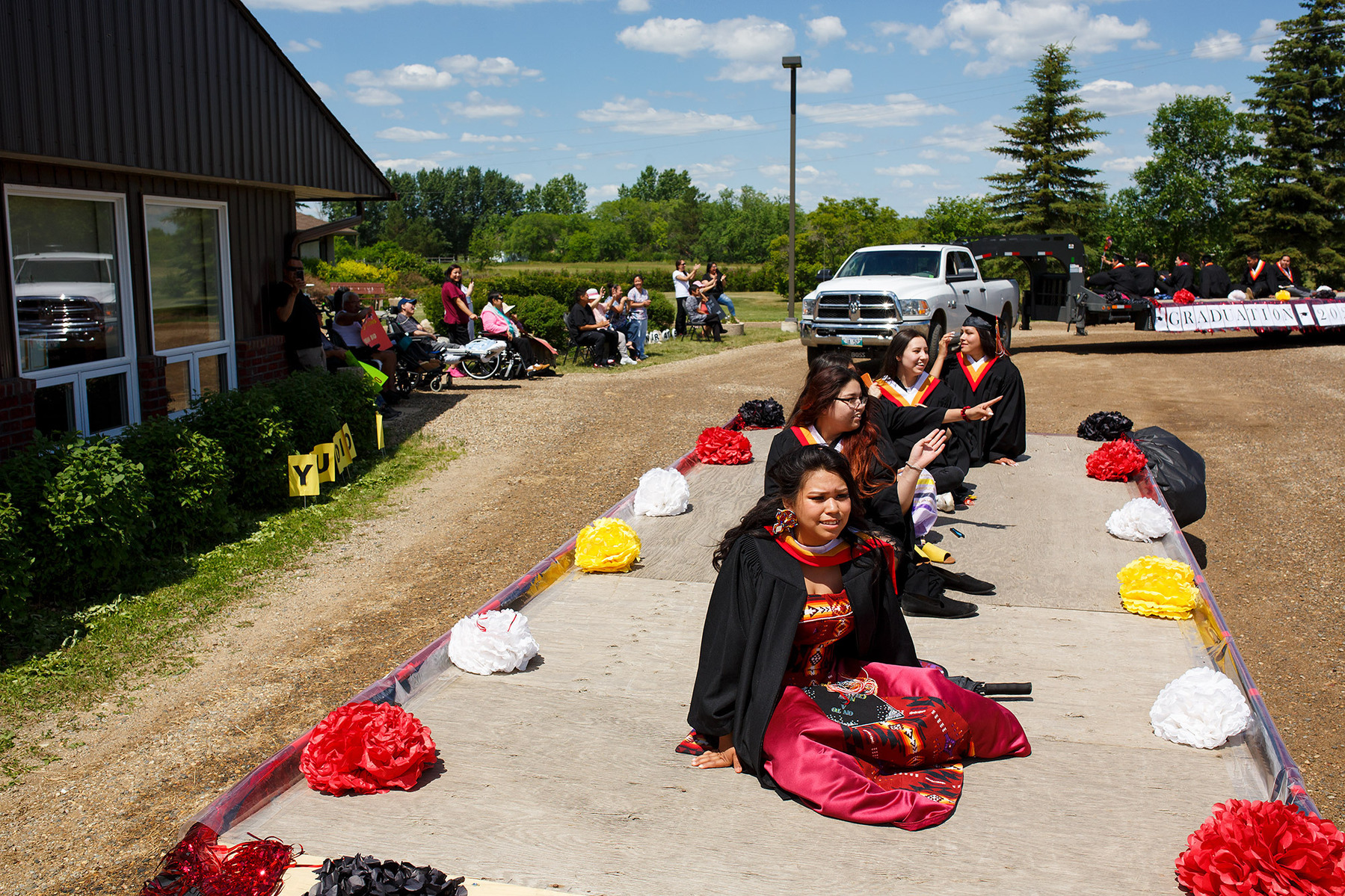 High school graduates are paraded through Sioux Valley Dakota Nation on a pair of flat-bed trucks.
