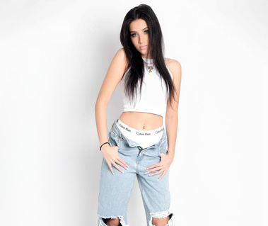 Studio portrait of a young woman with long dark hair, standing confidently in ripped jeans and a white crop top against a white background. Ideal for fashion branding, influencer content, and modeling portfolios in Arlington Heights and Chicago.
