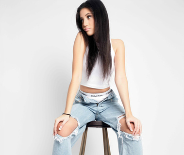 Studio portrait of a young woman with dark hair, wearing a white crop top and ripped jeans, sitting on a stool against a white background. A contemporary fashion look ideal for modeling portfolios, branding, and lifestyle photography in Arlington Heights 