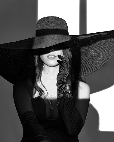 Black and white high-fashion portrait of a woman in a wide-brim hat, pearl necklace, and black gloves, partially veiled in shadow. Elegant and dramatic lighting makes this perfect for fine art, editorial, and luxury portrait photography in Arlington Heigh