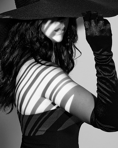 Black and white fine art portrait of a woman wearing a wide-brim hat and black gloves, with striped shadows cast across her face and shoulder. A cinematic, high-end photography style perfect for editorial, fashion, and creative branding in Arlington Heigh
