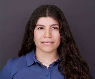 Corporate headshot of a woman with long wavy dark brown hair, wearing a blue polo against a neutral gray background. Ideal for executive branding, personal branding, and professional networking in Arlington Heights and Chicago.