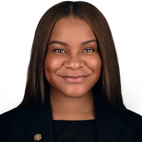 Confident business headshot of a young professional woman, wearing a black blazer with a pin, set against a white background. Perfect for corporate branding, leadership profiles, and business headshots in Arlington Heights and Chicago.