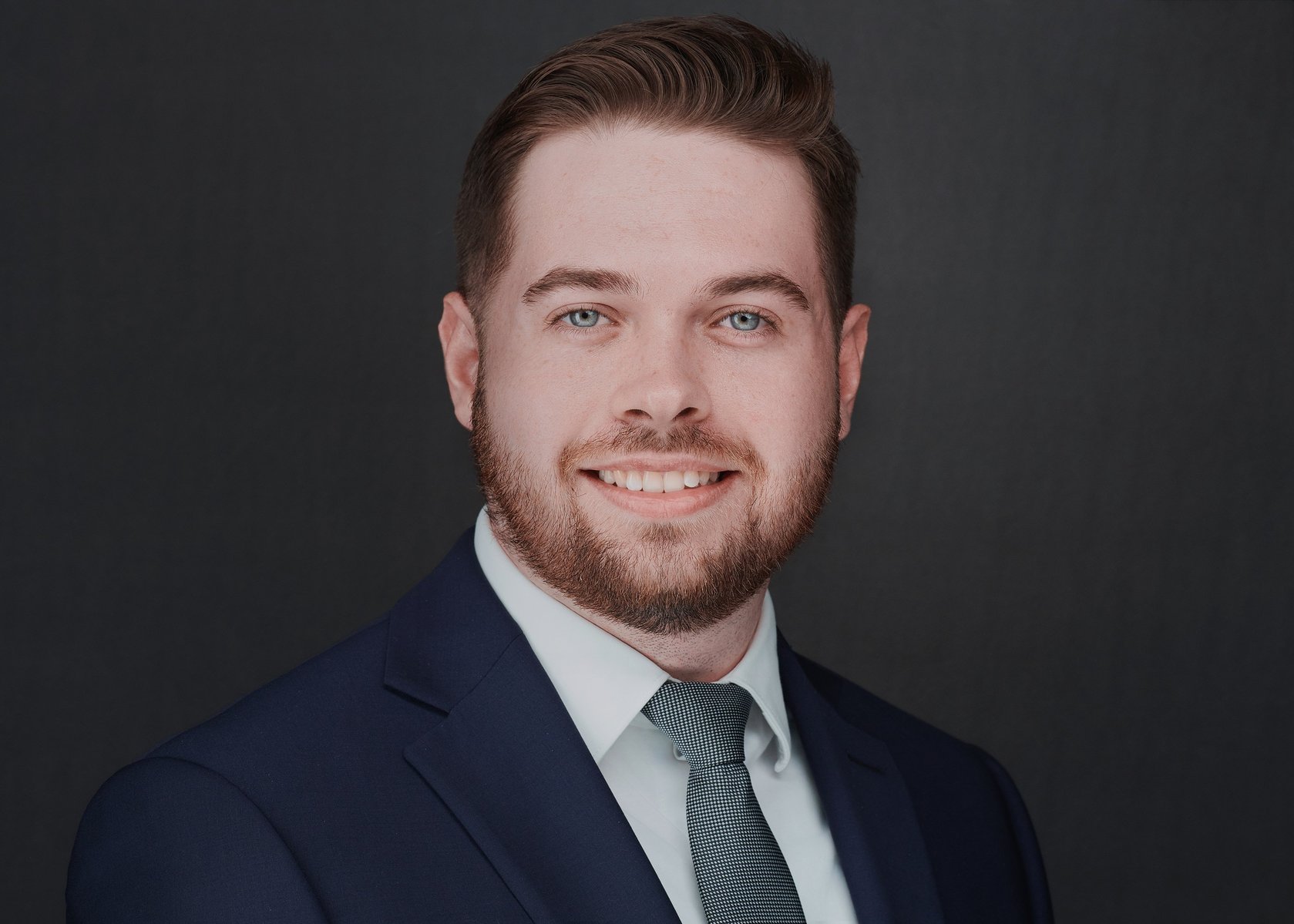 Professional headshot of an individual with a neutral background, dressed in business attire, displaying a clear and approachable expression