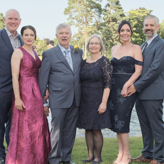 A well-dressed family poses outdoors in elegant attire with a scenic lake and greenery in the background. Perfect for wedding photography, formal event coverage, and professional family portraits in Arlington Heights and Chicago.