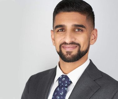 Corporate headshot of a man with short dark hair and a well-groomed beard, wearing a gray suit, white shirt, and patterned tie against a light gray background. Ideal for LinkedIn profiles, executive branding, and leadership portraits in Arlington Heights 