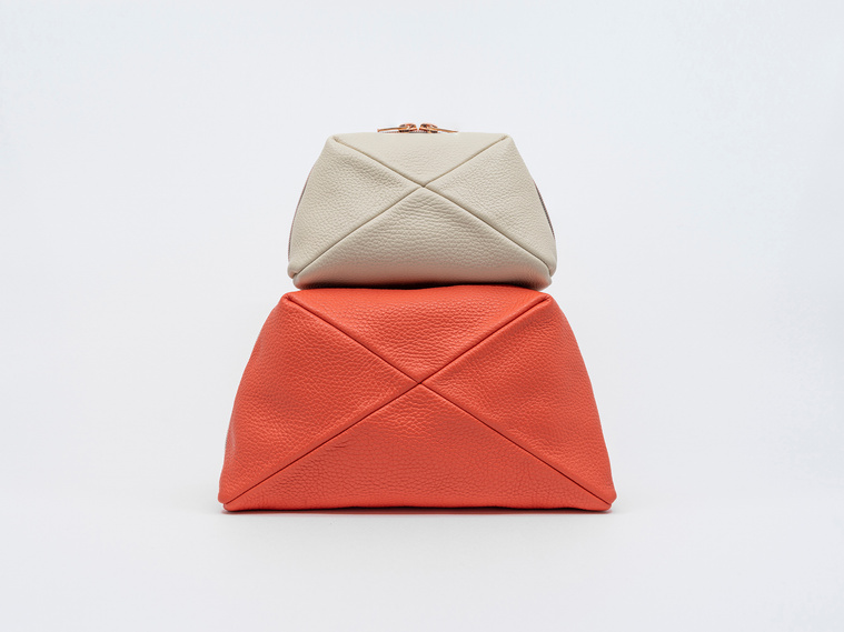 Handmade luxury leather cosmetic bags in two sizes, crafted in Delft, Netherlands. The Stella clutch features a unique geometric design, premium textured leather, and elegant rose gold zips. Colours: coral and sandy beach.