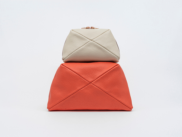 Handmade luxury leather cosmetic bags in two sizes, crafted in Delft, Netherlands. The Stella clutch features a unique geometric design, premium textured leather, and elegant rose gold zips. Colours: coral and sandy beach.