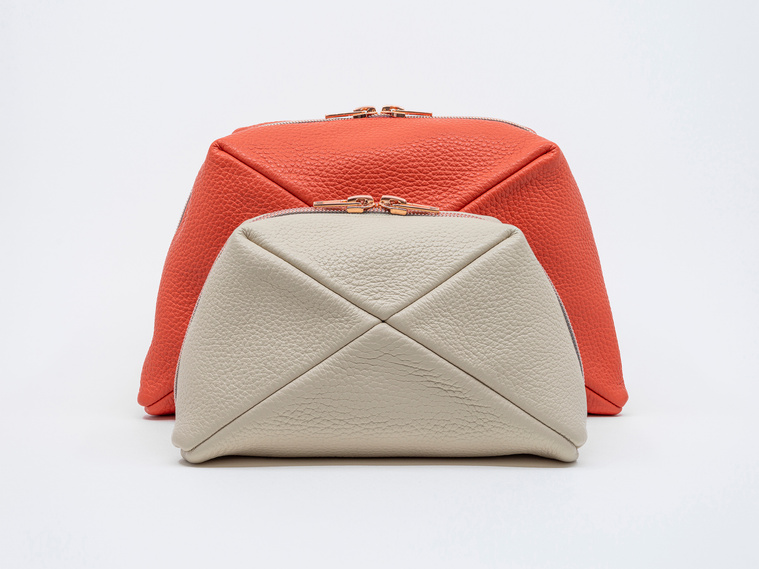 Handmade luxury leather cosmetic bags in two sizes, crafted in Delft, Netherlands. The Stella clutch features a unique geometric design, premium textured leather, and elegant rose gold zips. Colours: coral and sandy beach.
