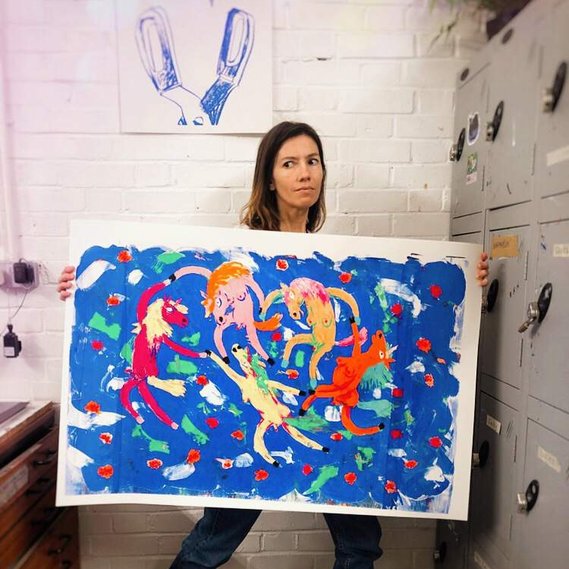 lowbrow pop artist Fabi Santiago holding her 'Matisse Dreams' painting with dancing naked unicorns.