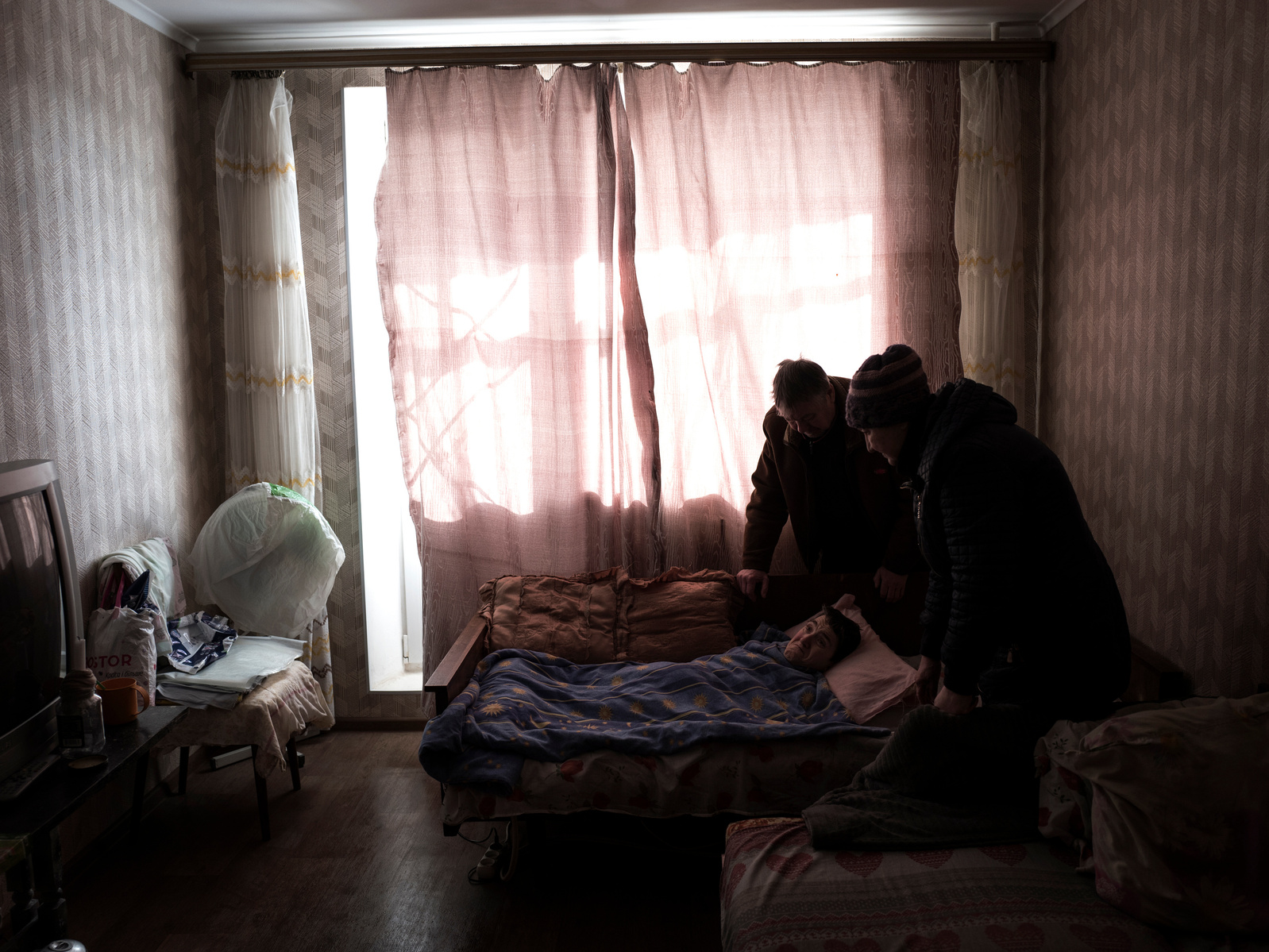 Natalia and Nicolai check on their quadriplegic daughter Oksana, 47. They flee Donbass region at the outbreak of war in 2014 only to be caught up again by war in an now bombed part of Kharkiv. Food and medicine delivery by volunteers at the front line dis