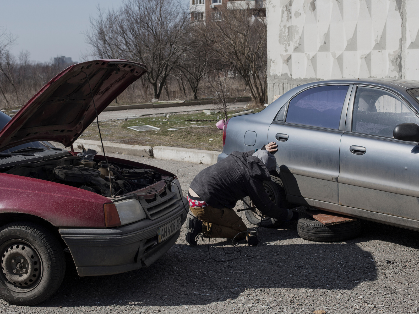 A man changing a flat tire on a car. Car repair and mechanic shops are closed in Kharkiv. Front line district of Industrialnyi, an eastern suburb of Kharkiv damaged by periodic shelling from Russia army. Kharkiv under shelling by Russian army, Ukraine. 29