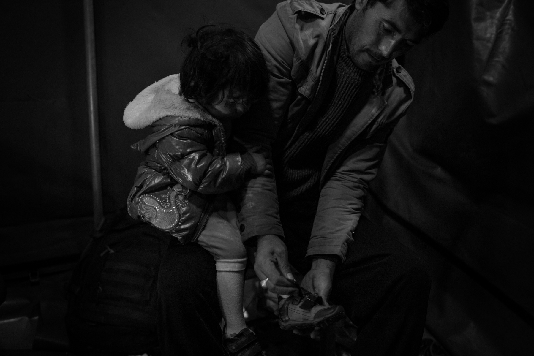 A man helps his young daughter with dry shoes in a tent set up by volunteers to welcome late incoming refugees from Afghanistan and Syria that landed at night on a rubber boat to the shores of Lesbos near Skala Sikaminias, Greece on 03 November, 2015. Les