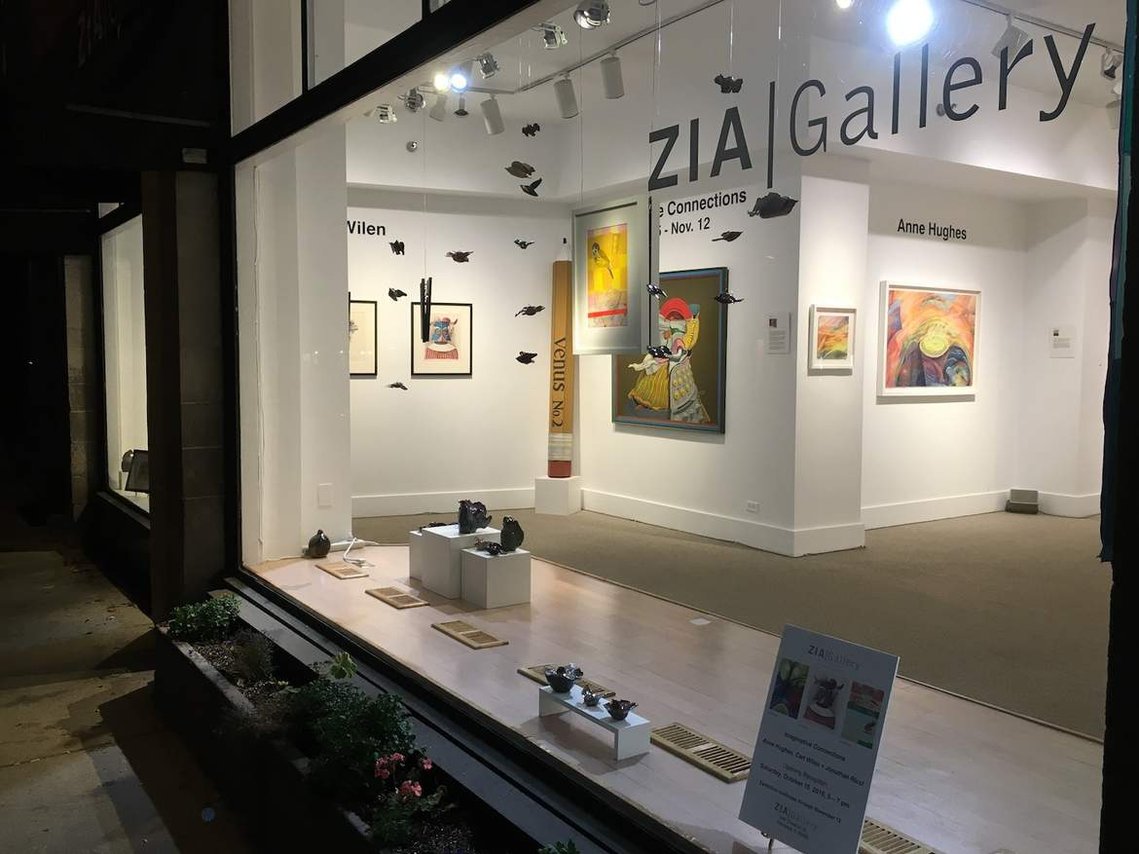 Photo of a gallery window at night with art on the walls and in the window.