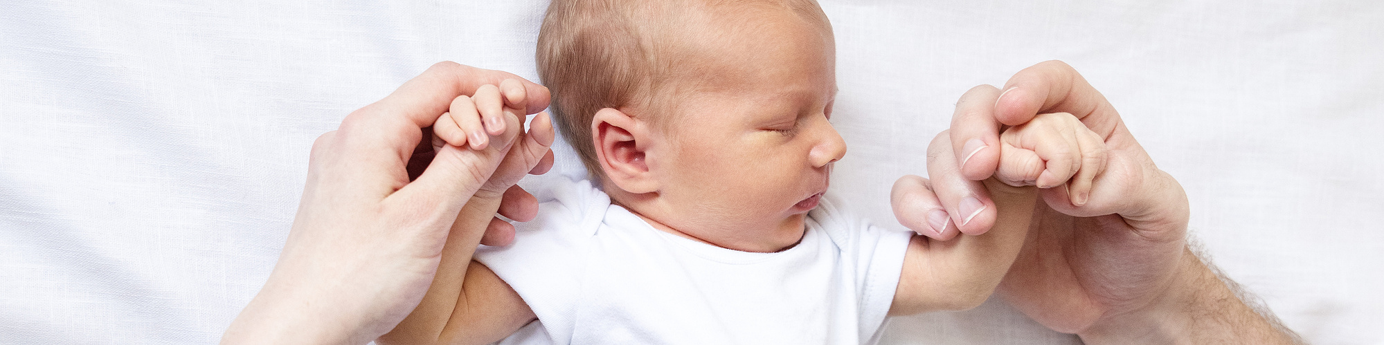 Newborn laying on white linen fabric, holding both parents hands in newborn photograph by professional newborn photographer Kids & Kin photography, Limerick, Ireland