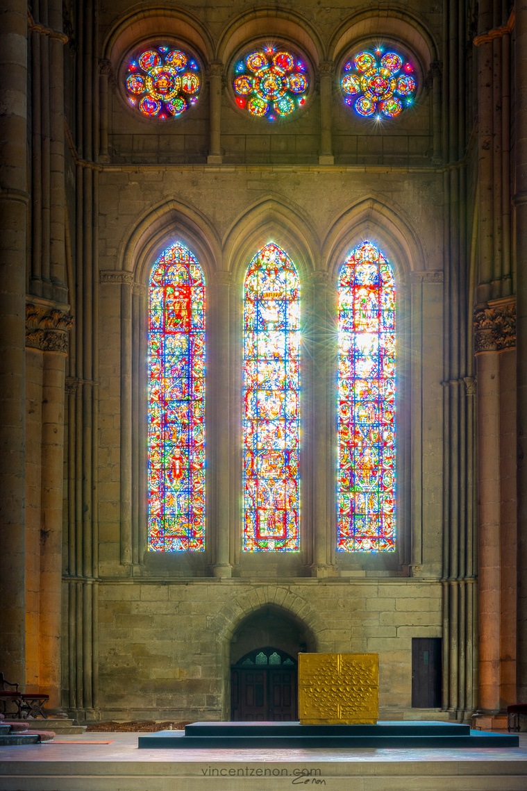 Les vitraux du champagne et les trois oculi hexalobés qui les surmontent dans le transept sud de la cathédrale de Reims, par une lumière chatoyante. L'autel central par devant.