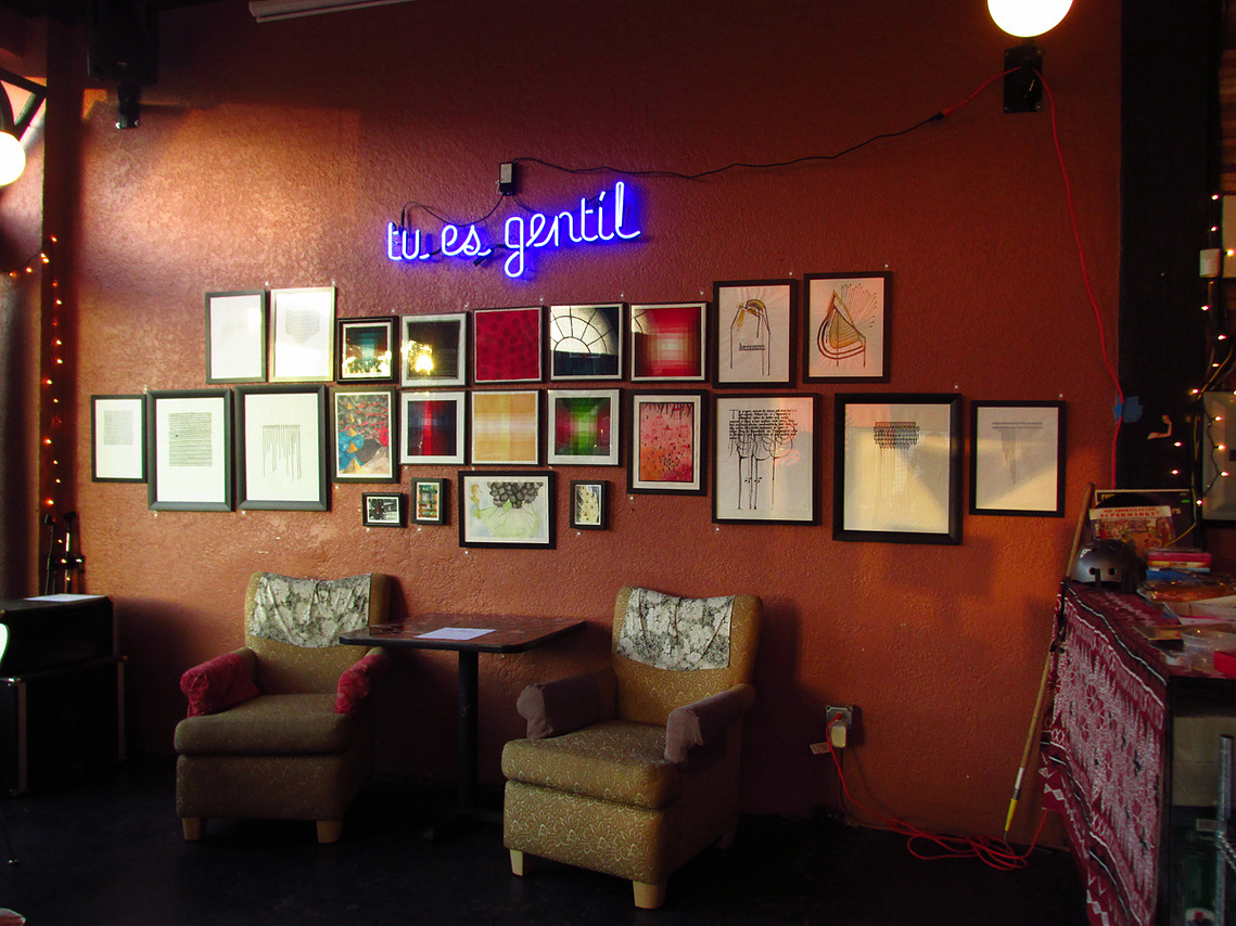 A muted orange colored wall is hung with a couple dozen paintings and the 