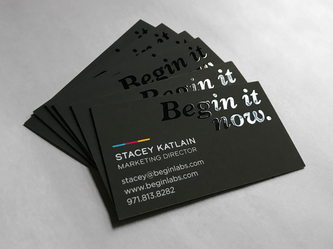The Begin Labs tagline in black glossy ink, printed on a stack of black business cards. 