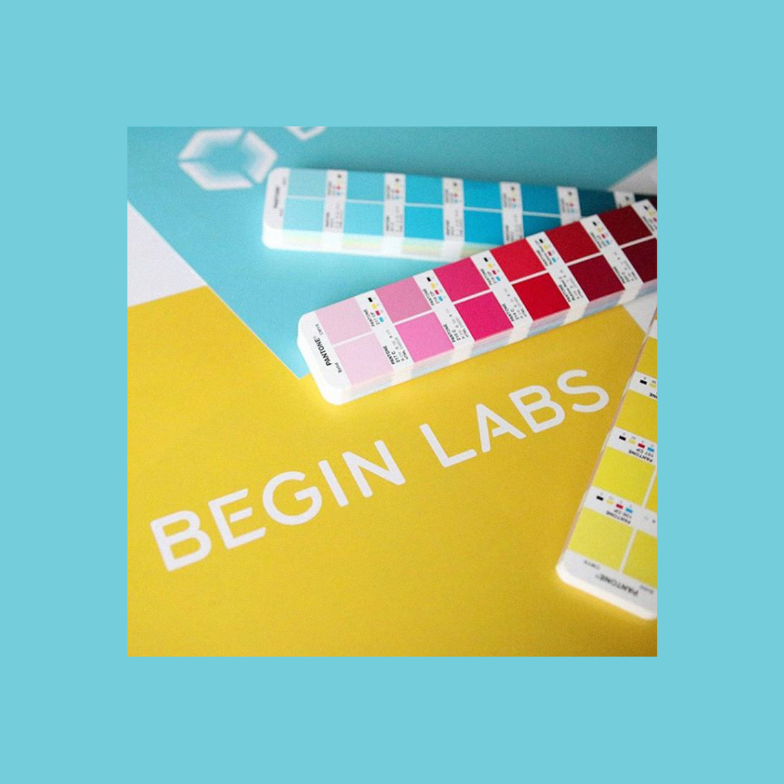 The Begin Labs logo in white on a yellow background with Pantone color booklet choices askew.