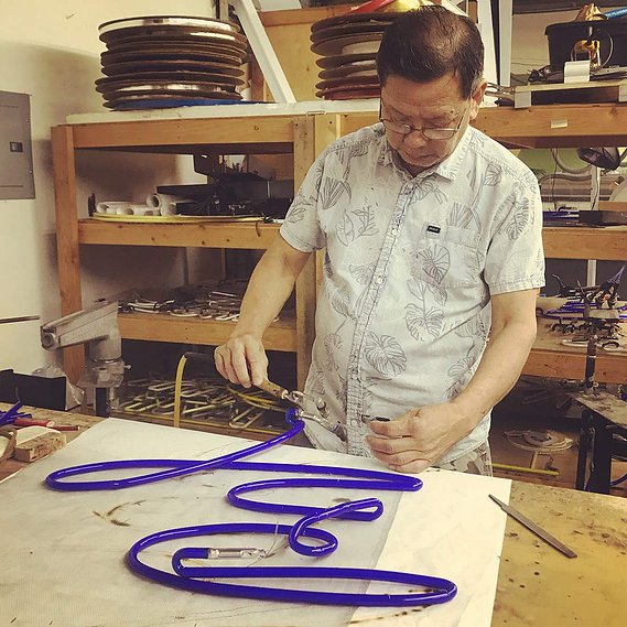 Peter Thanh Cao of Artico Lite  works with the electrodes on a blue neon tube bent in the design of script lettering. 