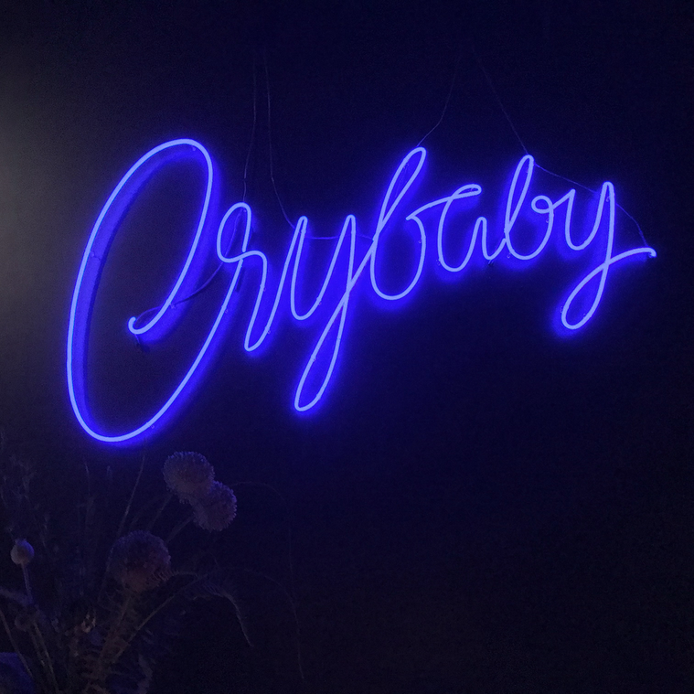 A lit neon sign, designed with expressive blue script lettering, spelling out the word 