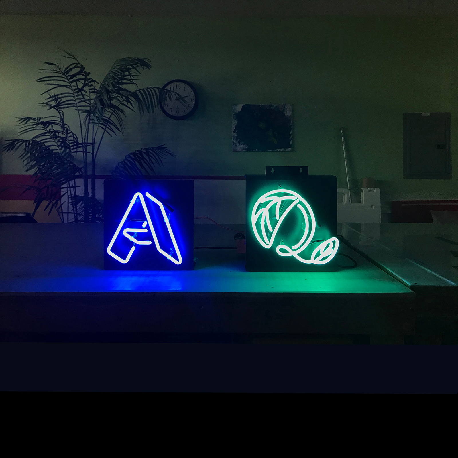 “A” and “Q” custom designed neon signs in blue and turquoise, each letter with a unique, fanciful typographic design.