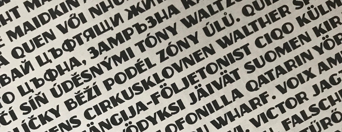 A dense type specimen of the Zaborsky font, at an angle with non-English words and phrases including many diacritic marks and Cyrillic characters. 