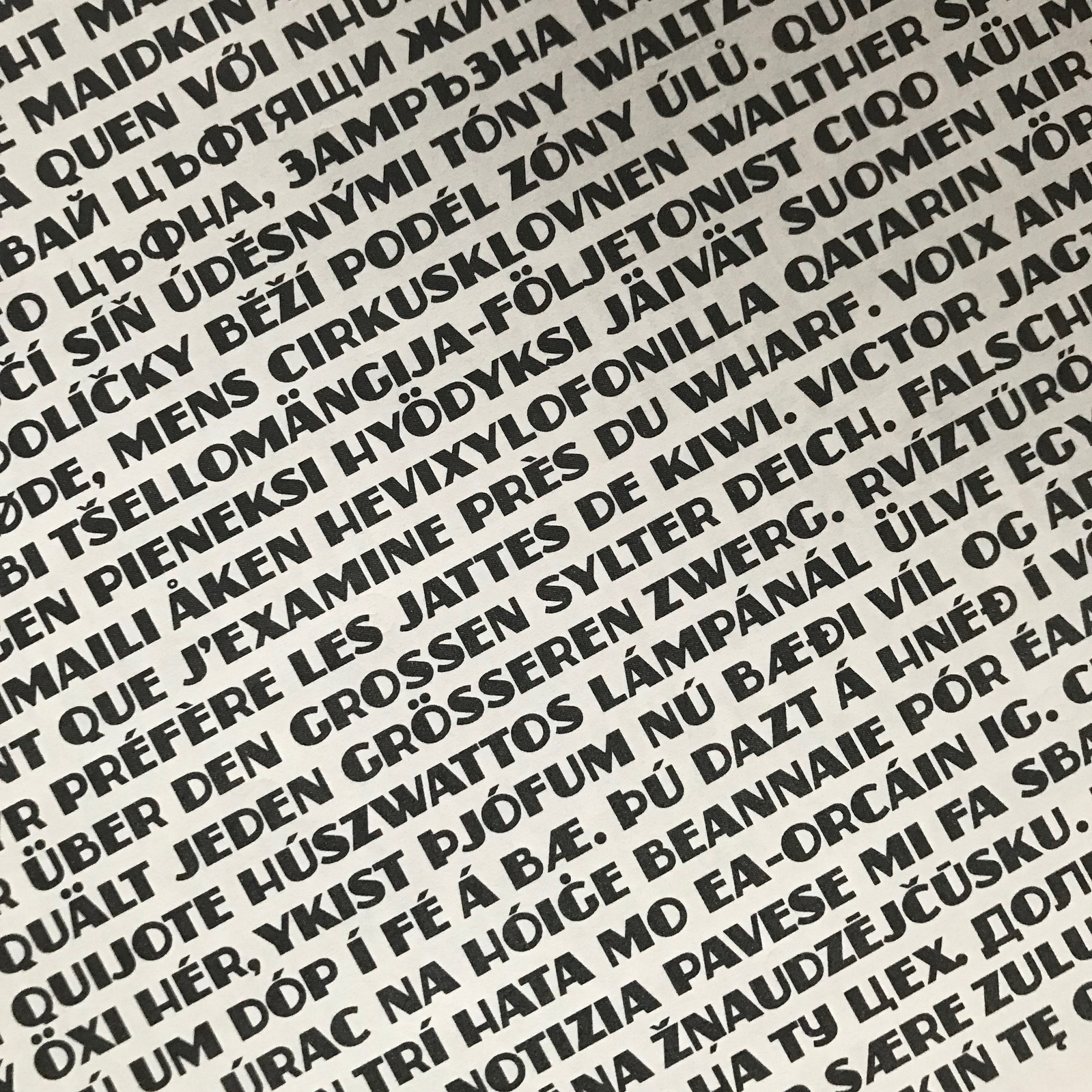 A dense type specimen of the Zaborsky font, at an angle with non-English words and phrases including many diacritic marks and Cyrillic characters. 