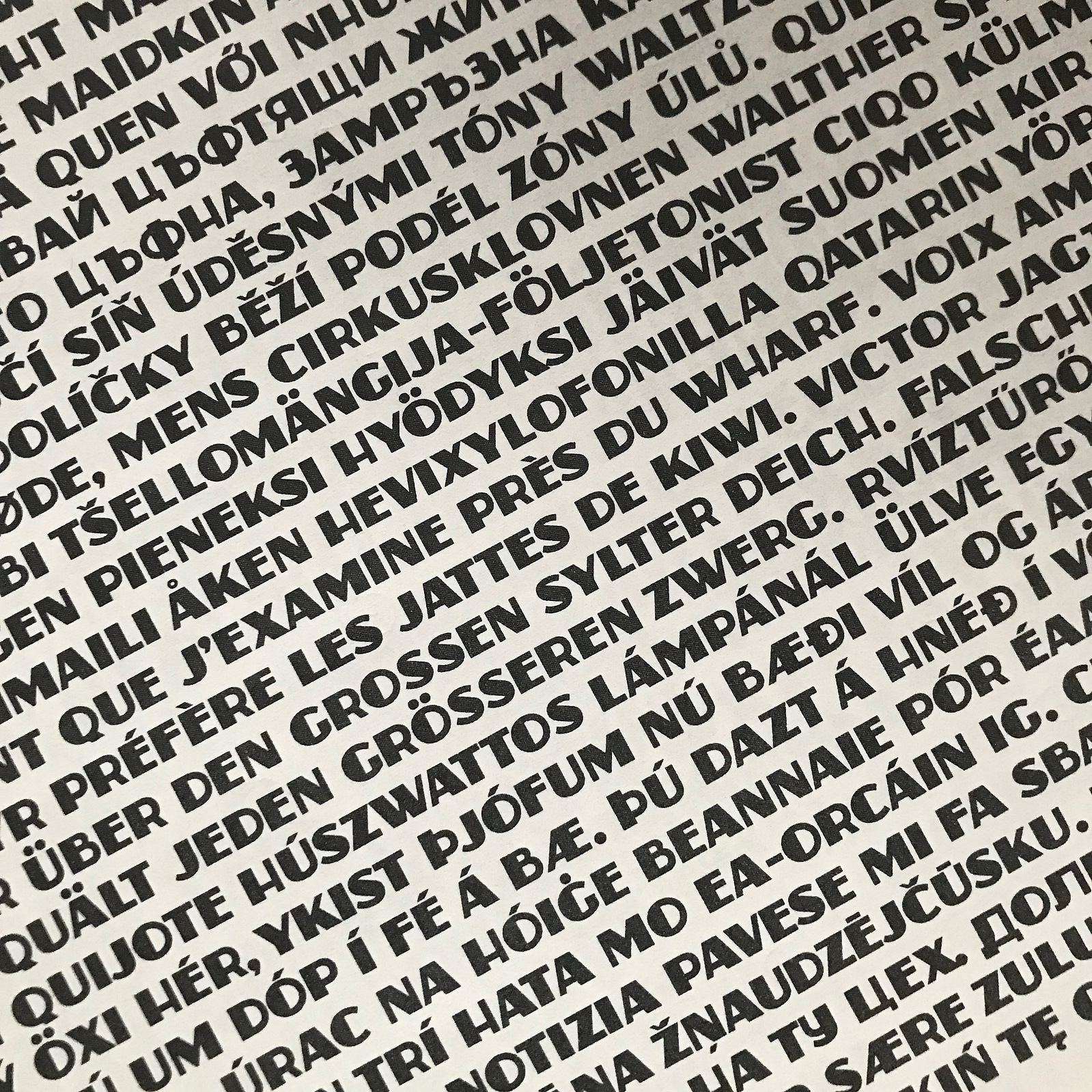 A dense type specimen of the Zaborsky font, at an angle with non-English words and phrases including many diacritic marks and Cyrillic characters. 